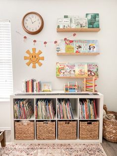 a bookshelf filled with children's books next to a wall mounted clock