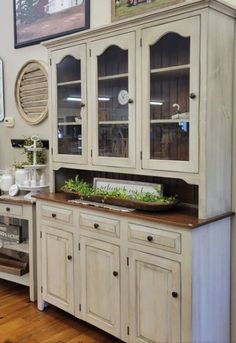 a white china cabinet with glass doors and drawers in a room filled with wood floors