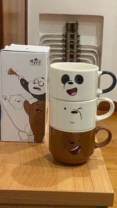 three coffee mugs sitting on top of a wooden table next to a boxed box