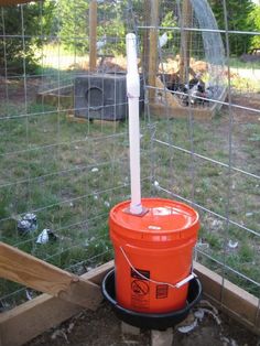 an orange bucket sitting in the middle of a fenced in area next to a chicken coop