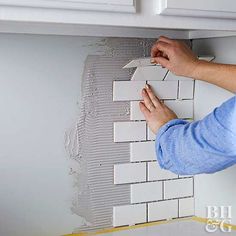 a man is working on a wall with white tiles and gray grouting around it