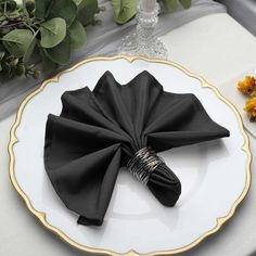 a white plate topped with black napkins on top of a table next to flowers