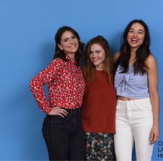 three women standing next to each other in front of a blue wall with one smiling at the camera