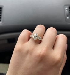 a woman's hand is holding an engagement ring in her left hand while she sits in the driver's seat of a car