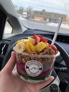 a person is holding up a bowl of fruit and granola in their hand while driving