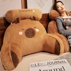 a woman is sitting next to a giant teddy bear and holding a magazine in her hands