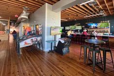 the inside of a sports bar with wooden floors and tables, stools, and televisions