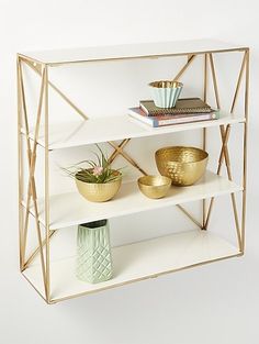 three shelves with gold vases and books on them, against a white wall background