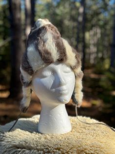 a white mannequin head with a fur hat on it's head and trees in the background