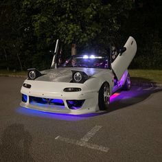 a white sports car with its doors open and lights on at night time in the parking lot