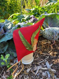 a red hat with green leaves on it sitting in the middle of some leafy plants