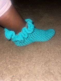 a woman's feet wearing blue crocheted slippers with ruffles on them