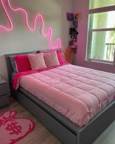 a bed with pink comforter and pillows in a room that looks like it has neon lights on the headboard