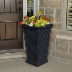 a black trash can sitting in front of a door next to a flower pot filled with flowers