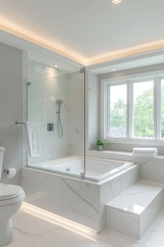 a white bathroom with a tub, toilet and window in the corner is lit by recessed lighting