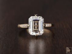 an emerald - cut diamond ring sits on a wooden surface