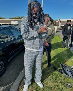 a man with dreadlocks standing in the grass next to a car and people