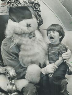 a young boy sitting next to santa clause in front of a christmas tree with his mouth open