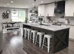 a large kitchen with white cabinets and counter tops, along with bar stools that match the hardwood flooring