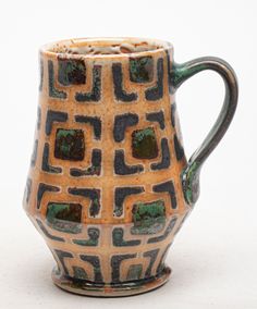 a brown and black cup with green designs on the inside is sitting on a white surface