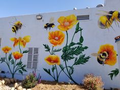 a painted wall with yellow flowers and bees on it's side next to a building