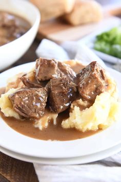 a white plate topped with mashed potatoes and beef on top of gravy