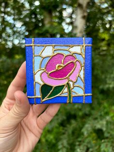 a hand holding up a small stained glass piece with a flower on it's side