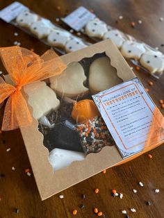 an orange ribbon is tied around some cookies in a box on a table with sprinkles