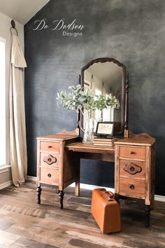 a wooden desk with a mirror on top of it next to a suitcase and flowers