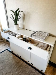 a white cabinet with drawers and plants in it next to a rug on the floor