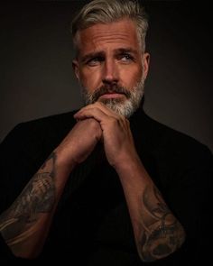 a man with grey hair and tattoos on his arms is looking at the camera while wearing a black shirt