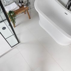 a white bath tub sitting on top of a bathroom floor next to a wooden table