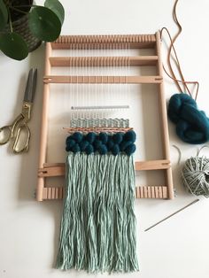 a weaving machine with yarn and scissors on the table next to it is a plant