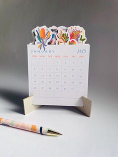 a desk calendar with colorful stickers on it next to a pen and paper holder