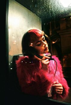 a woman with red hair talking on a cell phone while wearing a pink fur coat