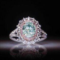 a fancy ring with an oval green diamond surrounded by white and pink diamonds on a black background