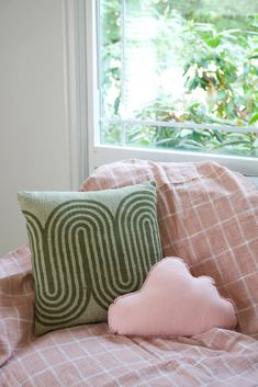 a pink pillow sitting on top of a bed next to a window