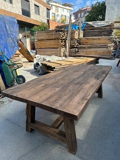 a wooden table sitting on top of a cement floor next to piles of wood planks