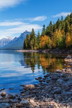 a lake surrounded by rocks and trees with mountains in the background