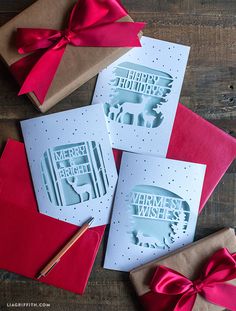 three greeting cards with bows and envelopes on a wooden table next to two wrapped presents