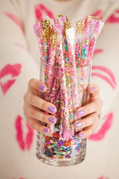 a woman holding a glass filled with lots of confetti and sprinkles