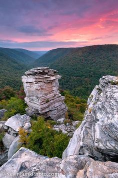 the sun is setting over some rocks in the mountains with trees and bushes on each side