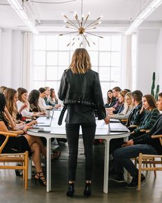 a woman standing in front of a group of people at a table with laptops