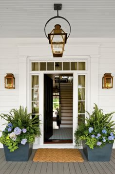 the front entrance to a house with potted plants and a lantern on the porch