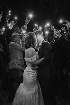 a bride and groom kissing in front of their wedding party with sparklers on their foreheads