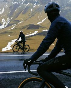 a person riding a bike on the road with mountains in the background