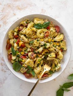 a bowl filled with pasta and vegetables on top of a white table next to a green leafy plant