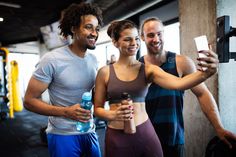 two men and a woman taking a selfie with their cell phones in the gym