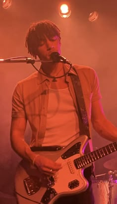 a man with dreadlocks playing an electric guitar in front of a microphone on stage