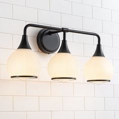 three light bathroom fixture with white and black glass shades on brick wall in public restroom